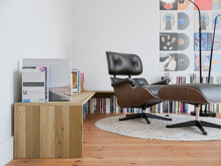 Modernes Wohnzimmer mit Parkettboden aus Eiche, einer Sitzbank aus Massivholz, einem Sessel mit Hocker und Regalen voller Bücher und Schallplatten.