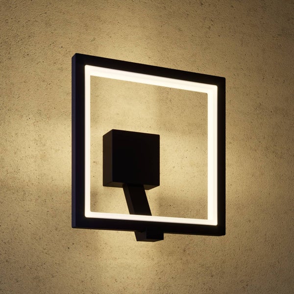 Quadratische LED-Wandleuchte in Schwarz mit leuchtendem Rahmen an einer strukturierten Wand.
