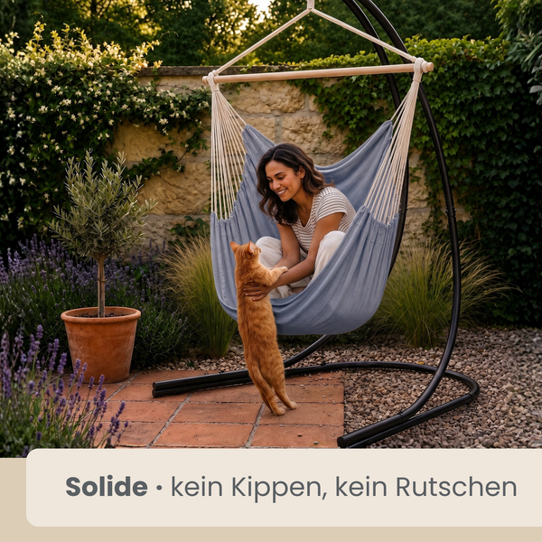 Frau sitzt entspannt in einer Hängematte mit Gestell im Garten und spielt mit einer Katze. Die Konstruktion steht stabil auf einer Terrasse.