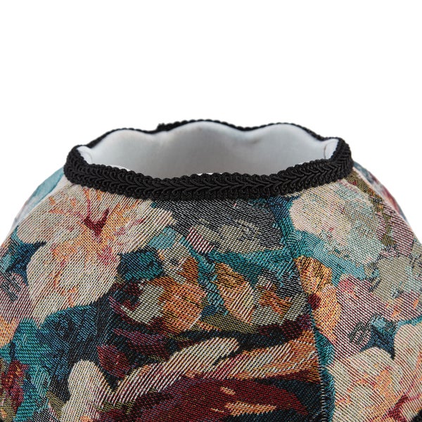 Nahaufnahme der oberen Kante eines gewebten Lampenschirms mit schwarzer Zierborte und buntem Gobelinmuster.