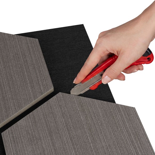 Eine Hand schneidet ein sechseckiges Wandpaneel mit Holzstruktur mit einem Cuttermesser zu.