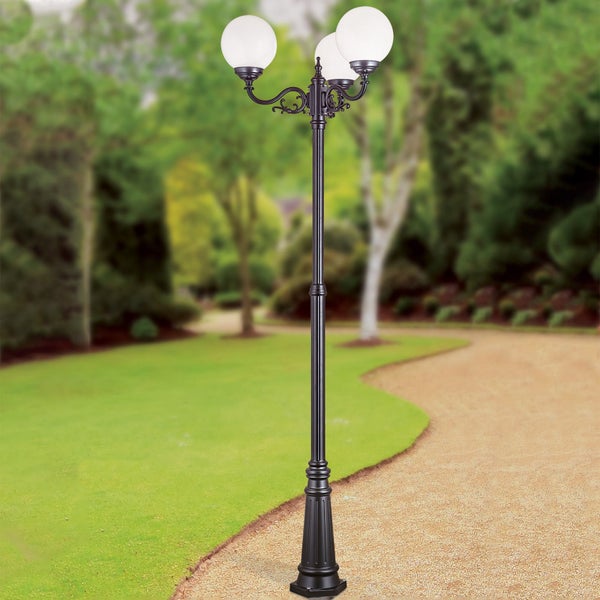 Klassische dreiflammige Gartenleuchte mit runden Glasschirmen auf einem verzierten Mast in einer hellen Gartenanlage mit Rasen und Kiesweg.