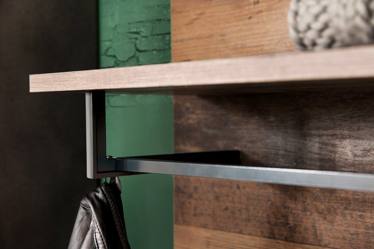 Wandgarderobe mit Paneelen in Holzoptik, Metallablage, Kleiderstange und Haken. Behangen mit Jacke und Kappe mit Adidas Logo vor einer Ziegelwand.