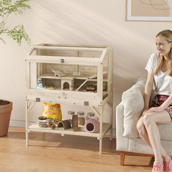 Kleintierstall aus hellem Holz mit Glasfronten und Ablagefach in einem hellen Wohnzimmer neben einem Sofa.
