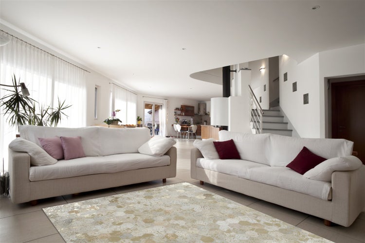 Helles und offenes Wohnzimmer mit zwei Sofas und einem gemusterten Teppich vor einer Treppe und einer Küche im Hintergrund.