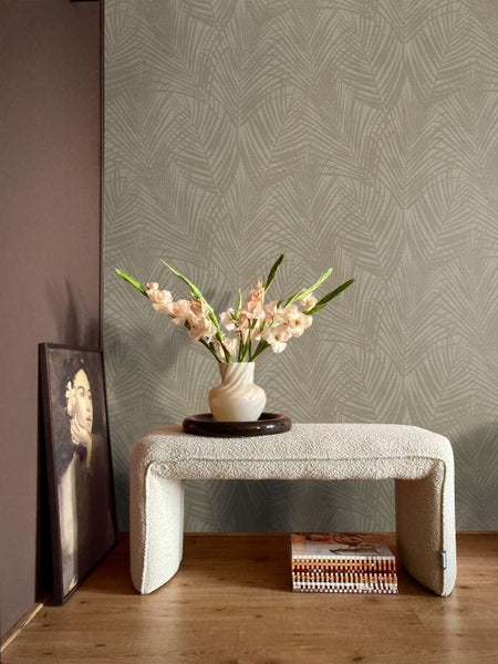 Wohnzimmer mit Vliestapete mit Palmenblattmuster, davor eine Sitzbank aus Boucle mit einer Blumenvase und einem gerahmten Bild.