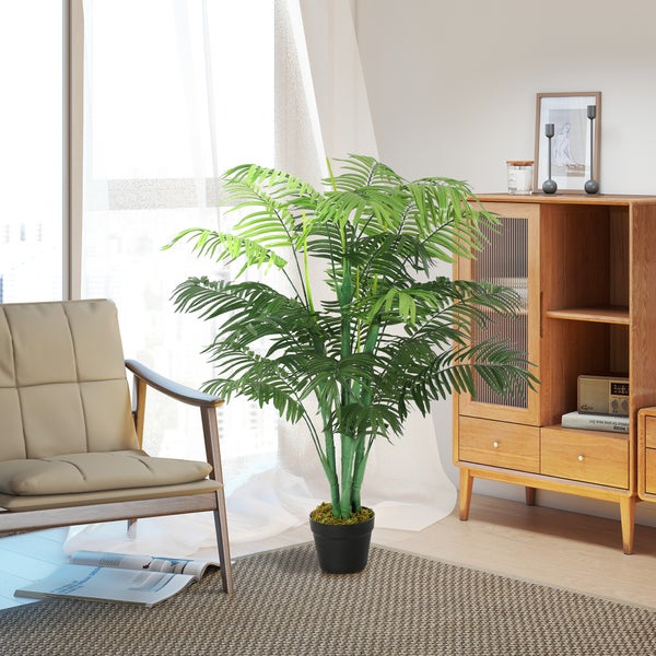 Künstliche Areca-Palme im schwarzen Topf in einem hellen Wohnzimmer mit Sessel und Holzschrank.