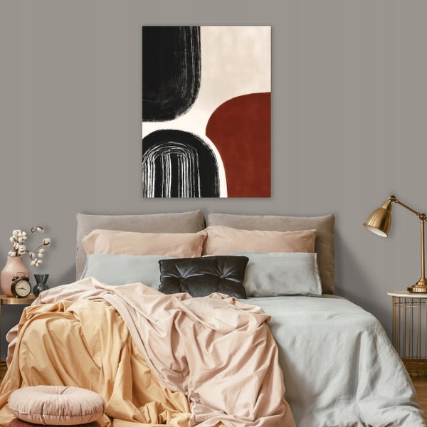Abstraktes Wandbild über einem modern eingerichteten Schlafzimmerbett mit Textilien in verschiedenen Tönen und metallischer Nachttischlampe