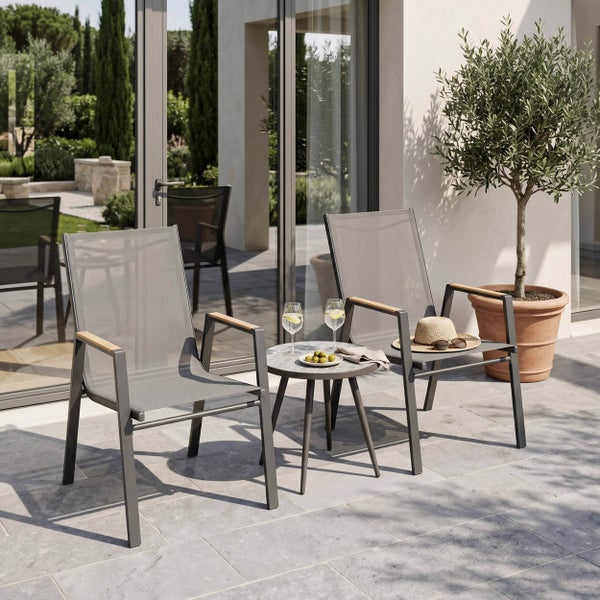 Moderne Gartengarnitur auf einer Terrasse mit zwei Gartenstühlen mit Netzbespannung und Holzarmlehnen sowie einem kleinen runden Beistelltisch.