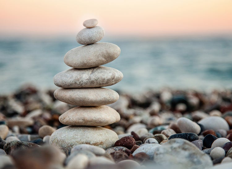 Stapel aus sieben flachen, hellen Kieselsteinen an einem Steinstrand am Meer.