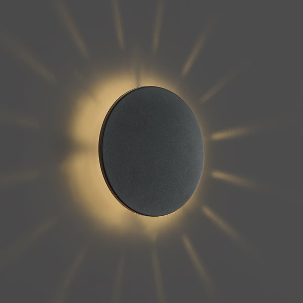 Runde schwarze Wandleuchte mit indirektem strahlenförmigem Lichteffekt an der Wand.