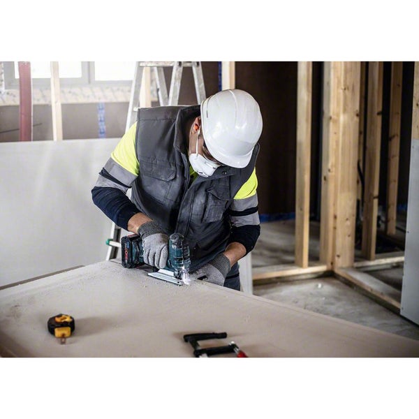 Ein Handwerker schneidet mit einer Stichsäge ein Werkstück in einer Werkstatt.