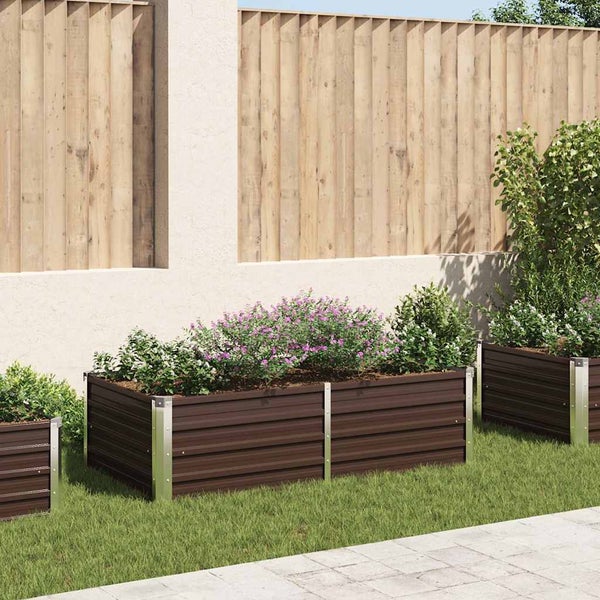 Rechteckiges Hochbeet aus Metall mit moderner Optik in einem Garten vor einem Holzzaun mit Pflanzen bepflanzt.