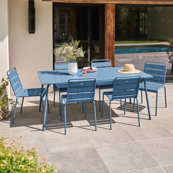 Moderner blauer Gartentisch mit sechs passenden Metallstühlen auf einer sonnigen Steinterrasse am Pool.