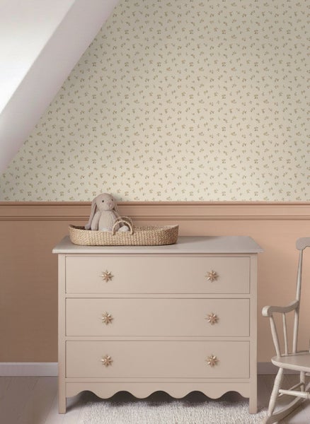 Kinderzimmer mit floral gemusterter Tapete, hellen Wandpaneelen, einer Kommode mit Sternenknöpfen und einem Plüschhasen in einem Korb.