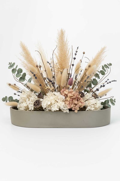 Trockenblumenarrangement in einer ovalen grauen Betonschale mit Pampasgras, Eukalyptus, Lagurus und Hortensien.
