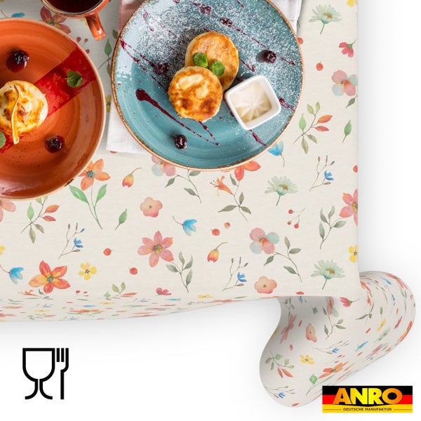 Abwaschbare Tischdecke mit Blumenmuster, eingedeckt mit Frühstück, ANRO DEUTSCHE MANUFAKTUR Logo, lebensmittelecht Symbol.