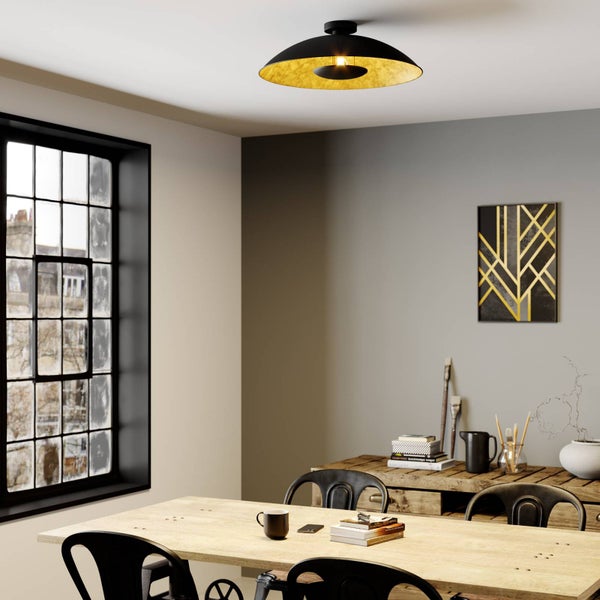 Schwarze Deckenleuchte mit goldener Innenseite in modernem Esszimmer über einem Holztisch mit schwarzen Stühlen und einem großen Fenster.