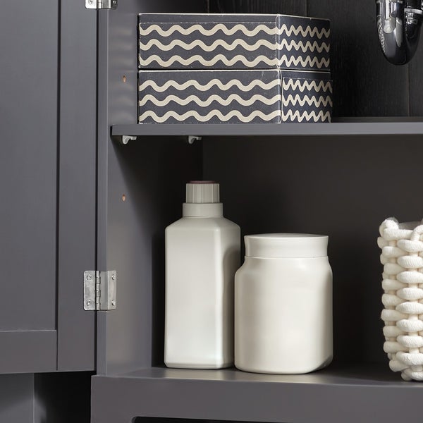 Detailaufnahme eines Badezimmerschranks mit Ablagefläche, auf der sich zwei Kartons, eine Flasche, ein Behälter und ein geflochtener Korb befinden.