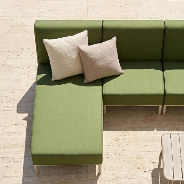 Modulare Gartenlounge in Grün mit zwei hellen Dekokissen auf einer Terrasse aus hellen Steinplatten.