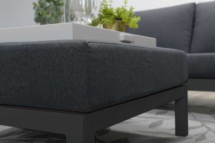 Moderner Loungehocker mit grauem Polsterkissen und einem weißen Tablett auf einem dunklen Aluminiumgestell.