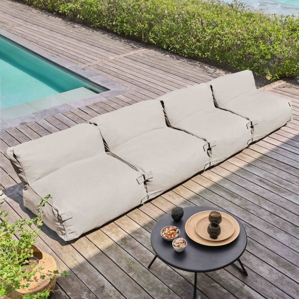 Modulares Outdoor-Sitzsack-Sofa in Hellgrau auf einer Holzterrasse neben einem Pool, inklusive kleinem schwarzem Beistelltisch.