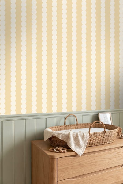 Tapete mit vertikalen Punktstreifen über einer grünen Wandverkleidung in einem hellen Kinderzimmer mit einer Wickelkommode aus Holz.