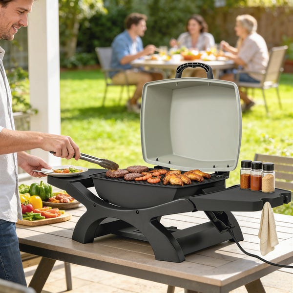 Elektrischer Tischgrill mit offenem Deckel auf Holztisch im Garten, belegt mit Grillgut, Personen im Hintergrund.