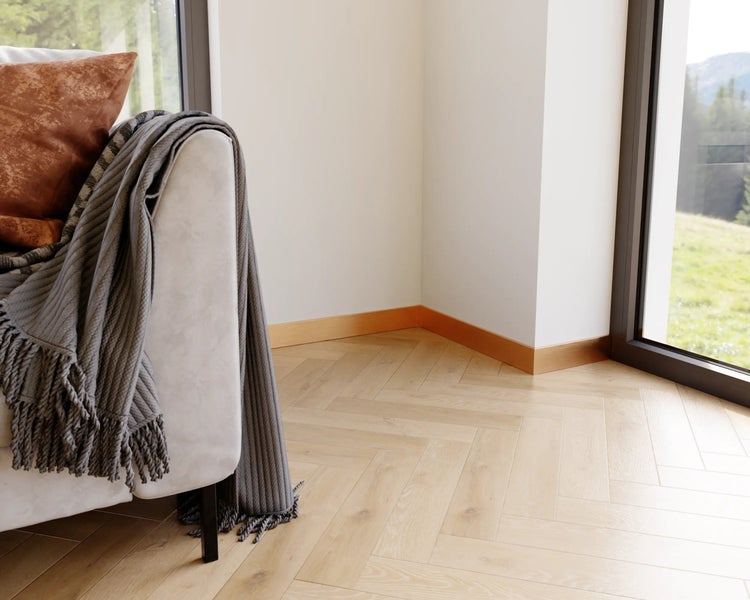 Detailaufnahme eines hellen Zimmers mit Fischgrätenparkett, einer Couch mit Kissen und Decke sowie einer großen Fensterfront.