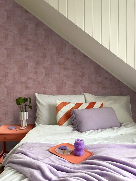 Schlafzimmer mit Bett, Nachttisch und dekorativen Accessoires unter einer Dachschräge.