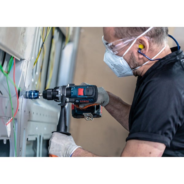 Handwerker bohrt mit einem Bosch Akku-Bohrschrauber ein Loch in eine Wand, geschützt durch Maske, Brille und Ohrstöpsel.