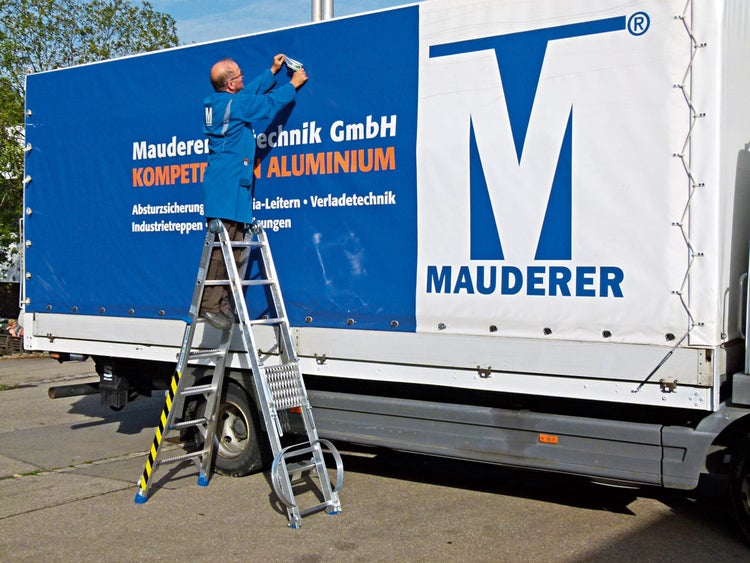 Mann auf einer Aluminium-Leiter vor einem Lastwagen mit Mauderer Technik GmbH Aufdruck.