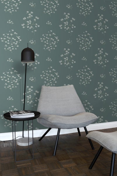 Wohnraum mit blumiger Tapete, Sessel, Fußhocker und Stehleuchte