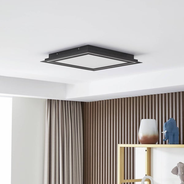 Quadratische LED-Deckenleuchte mit schwarzem Rahmen in einem modernen Raum mit Holzlamellenwand und beigen Vorhängen.