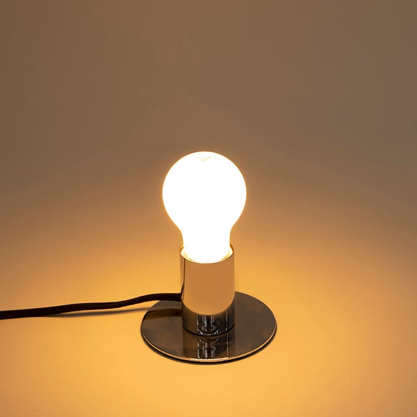 Moderne Tischleuchte mit verchromtem Standfuß, weißer Glühbirne und schwarzem Textilkabel.