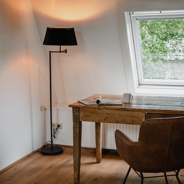 Innenaufnahme eines Zimmers mit Stehlampe, Holztisch, Sessel und Dachfenster.