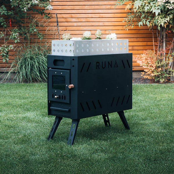 Schwarzer RUNA Outdoor-Ofen aus Metall auf einem grünen Rasen im Garten mit Holzzaun.