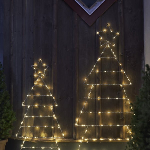 Zwei dekorative, beleuchtete Weihnachtsbäume an einer Holzwand