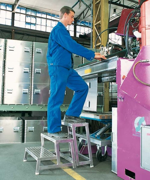 Mann auf einer dreistufigen Aluminiumleiter in einer Werkshalle.