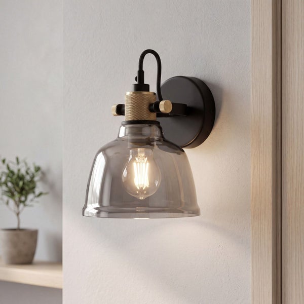 Wandlampe mit schwarzer Halterung, goldenen Akzenten und rauchgrauem Glasschirm. Montiert an einer hellen Wand.