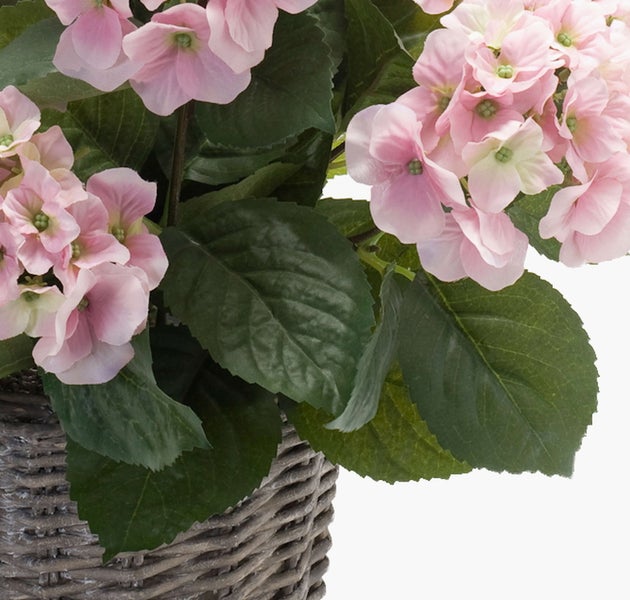 Künstliche Hortensie mit rosa Blüten und grünen Blättern in einem grauen Weidenkorb