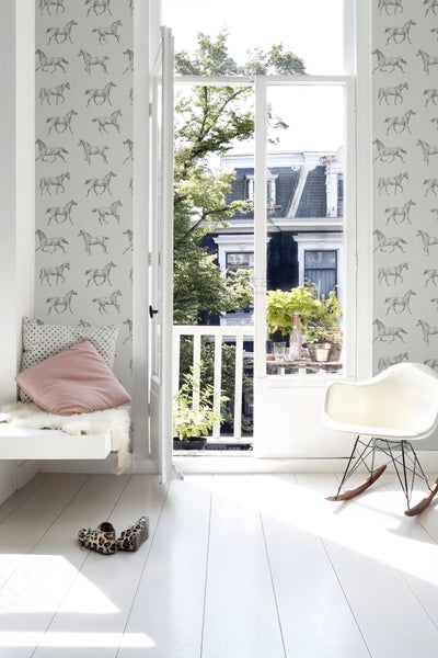 Heller Raum mit Pferdetapete, offenem Fenster zum Balkon, weißem Schaukelstuhl und Sitzbank mit Kissen