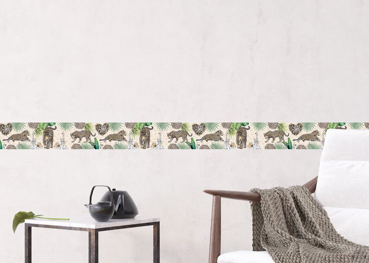 Selbstklebende Tapetenbordüre mit Leoparden- und Dschungelblatt-Motiv an einer hellen Wand über einem Beistelltisch und Sessel.