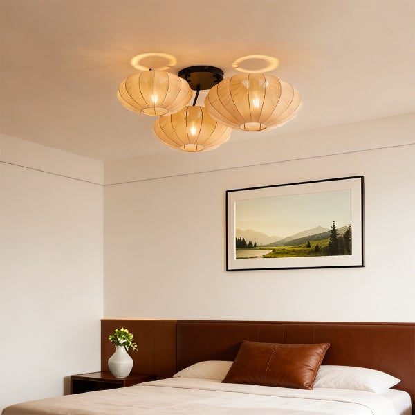 Dreiflammige Deckenleuchte mit beigen Textilschirmen in einem modern gestalteten Schlafzimmer mit braunem Lederkopfteil und Landschaftsbild.