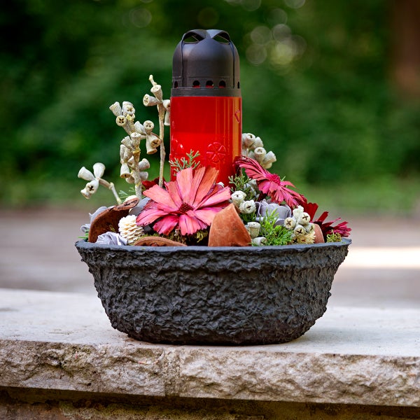 Gesteck mit roter Grableuchte in einer dunklen Pflanzschale