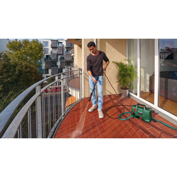 Eine Frau reinigt eine Terrasse aus Steinplatten mit einem Hochdruckreiniger in einem üppig bepflanzten Garten.