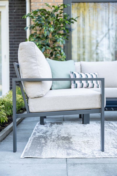Moderner Garten-Lounge-Sessel mit Metallrahmen in Anthrazit und hellen Polstern auf einem Außenteppich auf einer Terrasse.
