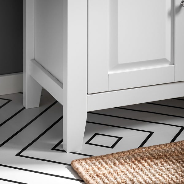 Detailansicht eines weißen Waschtischunterschranks mit Beinen und einer braunen Fußmatte auf einem Badezimmerboden mit geometrischem Muster.
