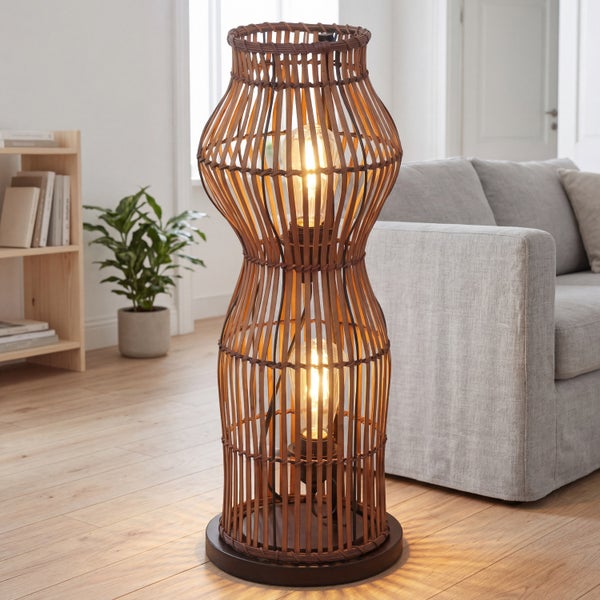 Stehleuchte aus geflochtenem Rattan in taillierter Form mit zwei leuchtenden Lampen in einem hellen Wohnzimmer neben einem grauen Sofa.