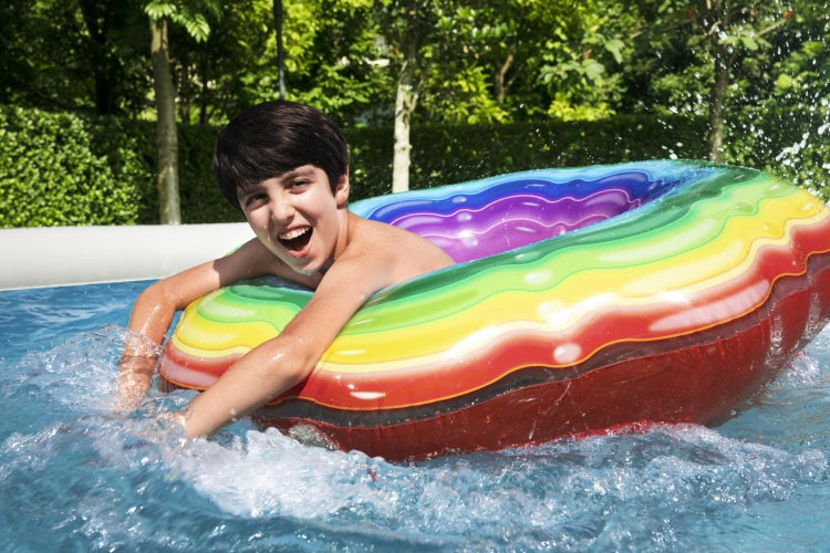 Kind mit buntem Regenbogen-Schwimmreifen in einem Swimmingpool.